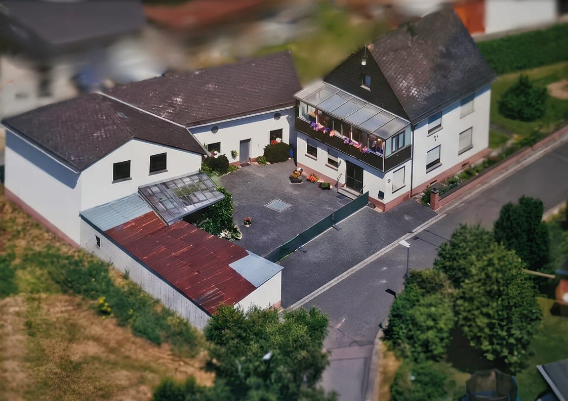 Luftaufnahme des Einfamilienhauses mit verglastem Balkon, Nebengebäude und gepflastertem Hof in Anschau